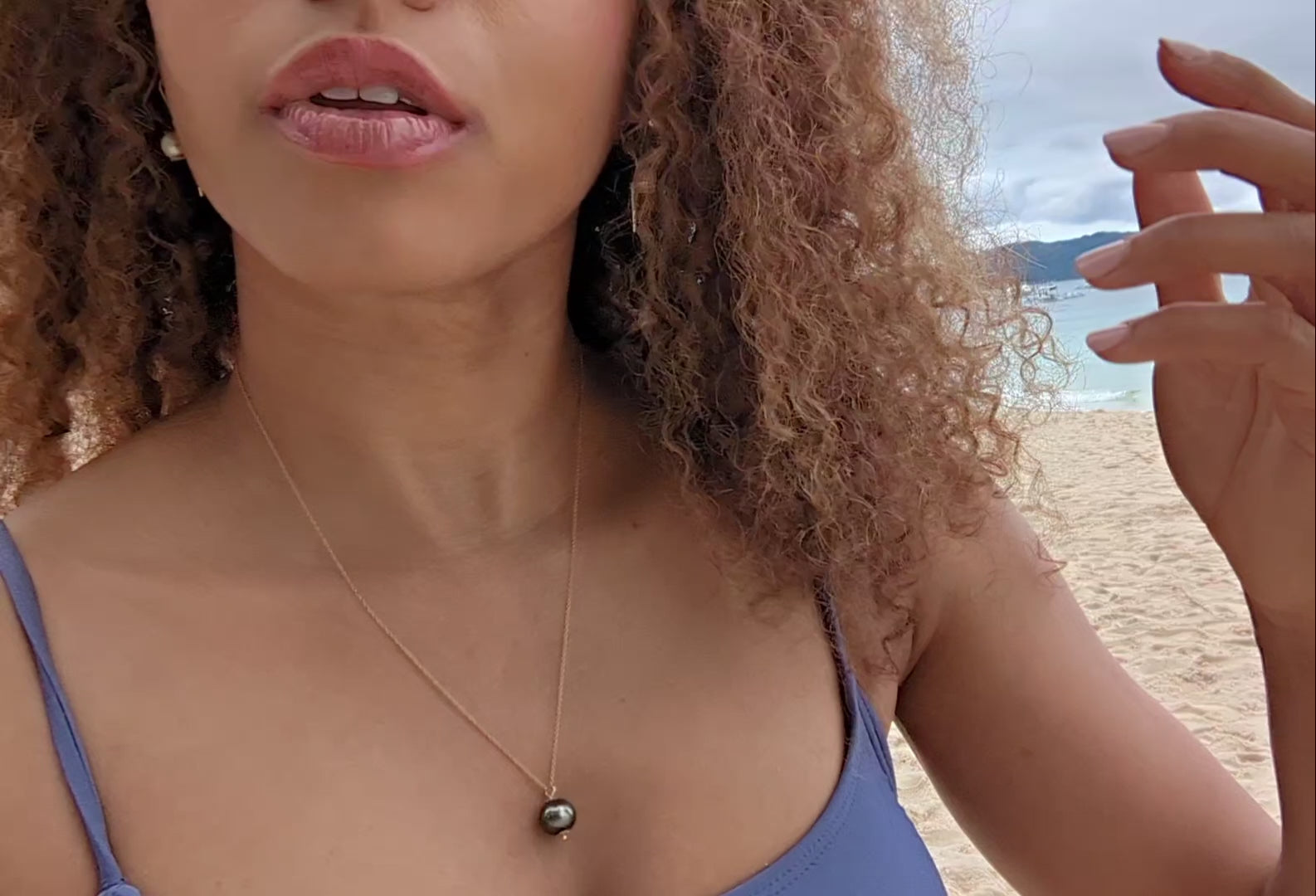 video of black woman with curly hair in a purple bikini on a beach wearing the black South sea pearl pendant from the wandering jewel