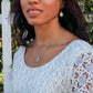 woman in bridal dress standing in front of a white picket fence wearing flower pendant necklace and matching earrings from the wandering jewel
