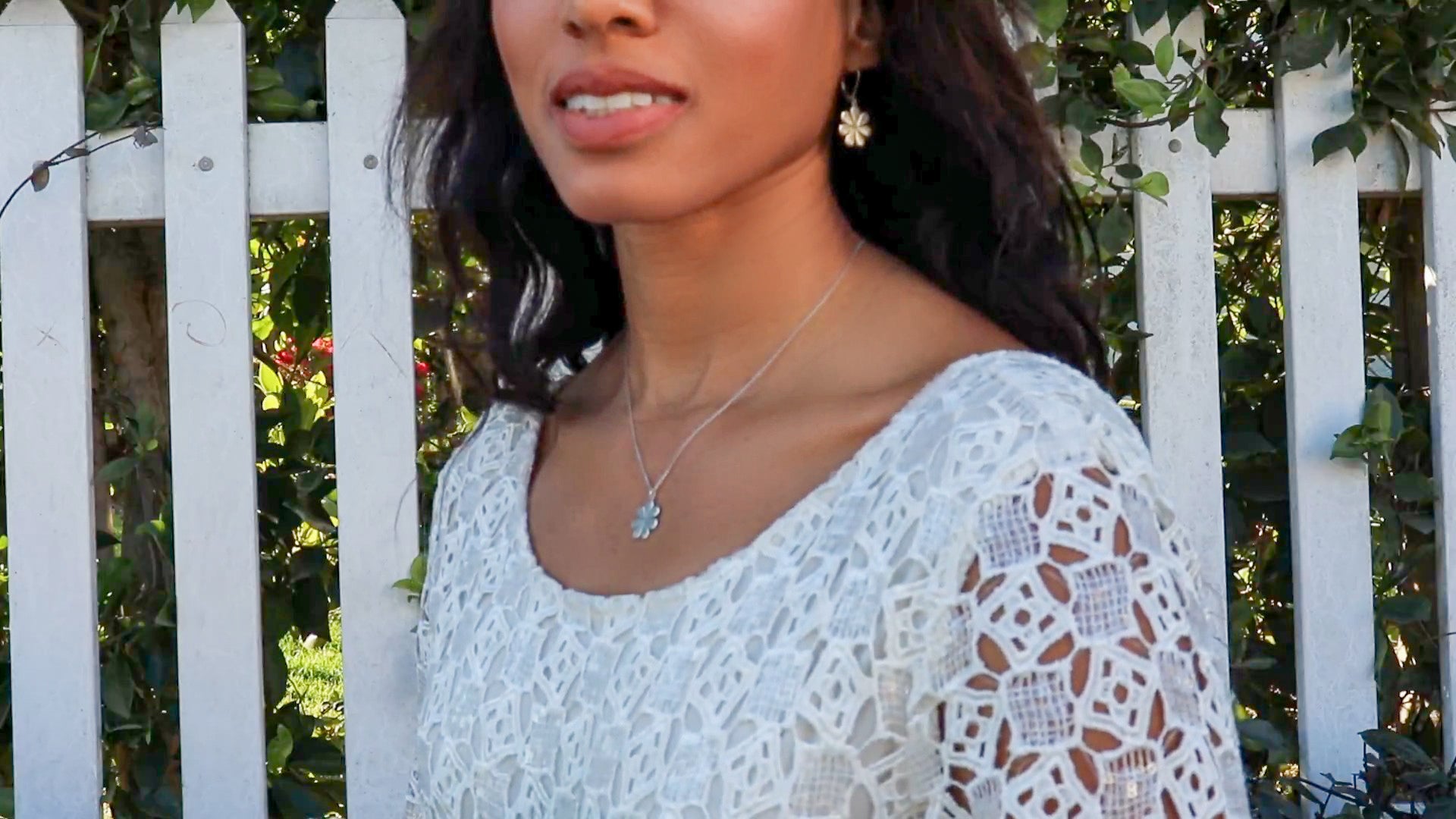 woman in bridal dress standing in front of a white picket fence wearing flower pendant necklace and matching earrings