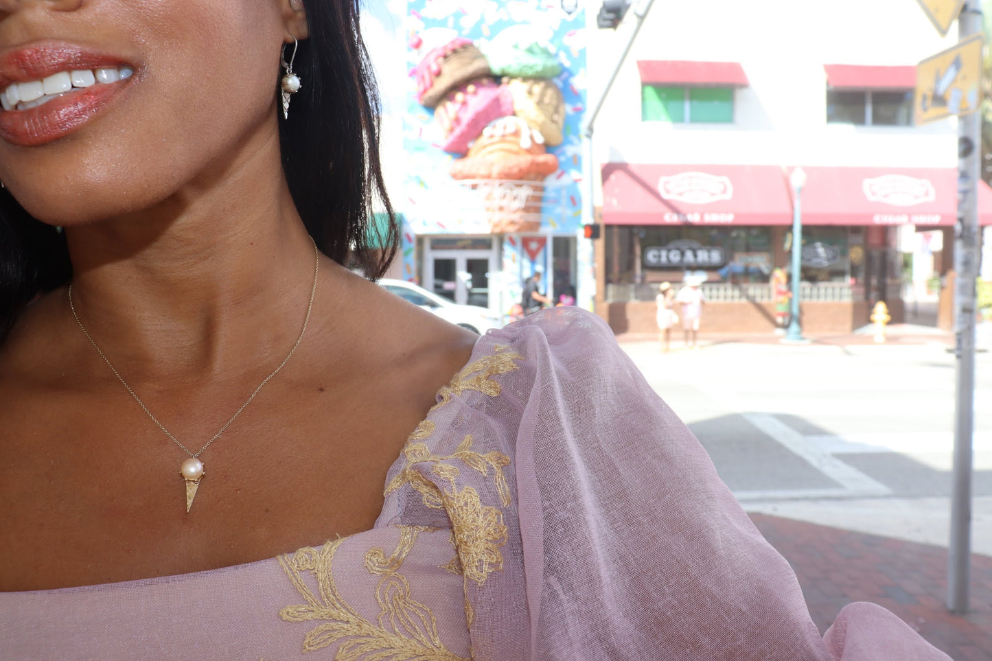 black woman in pink renaissance blouse standing in front of an ice cream parlor wearing an ice cream pearl pendant necklace from the wandering jewel
