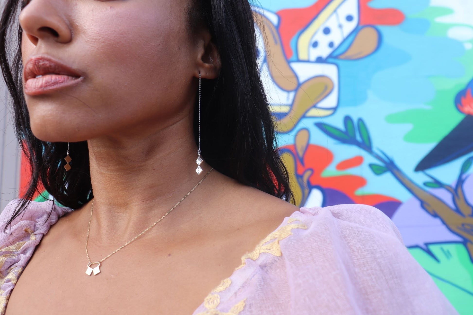 black woman in a pink puff sleeve renaissance blouse standing in front of a graffiti wall wearing dice earrings and a dice necklace from the wandering jewel