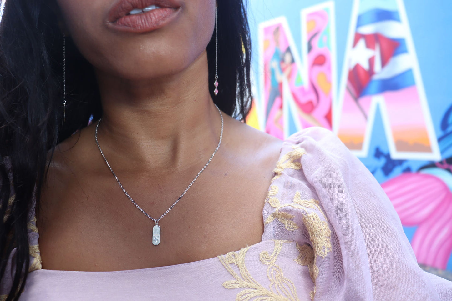 woman in front of graffiti wearing a small pill shaped pendant necklace from the wandering jewel