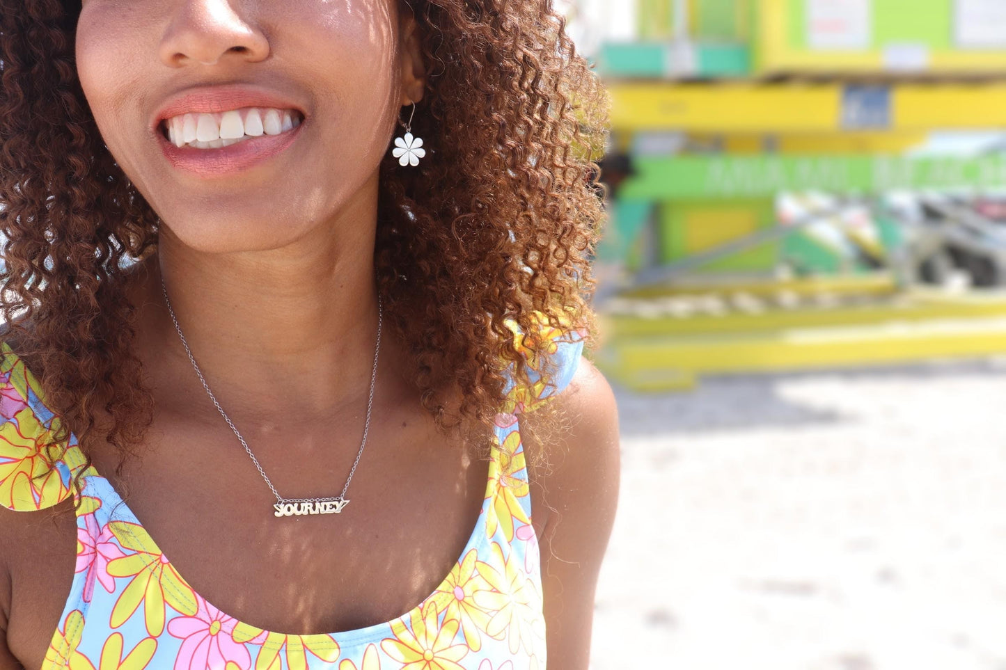 A smiling woman on the beach in a yellow bikini wearing a journey nameplate necklace