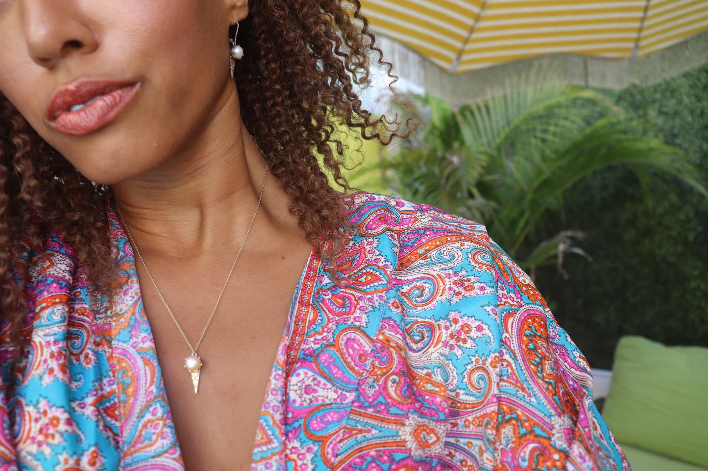 black woman in a blue and purple paisley robe at pool wearing an ice cream pearl pendant necklace and matching earrings