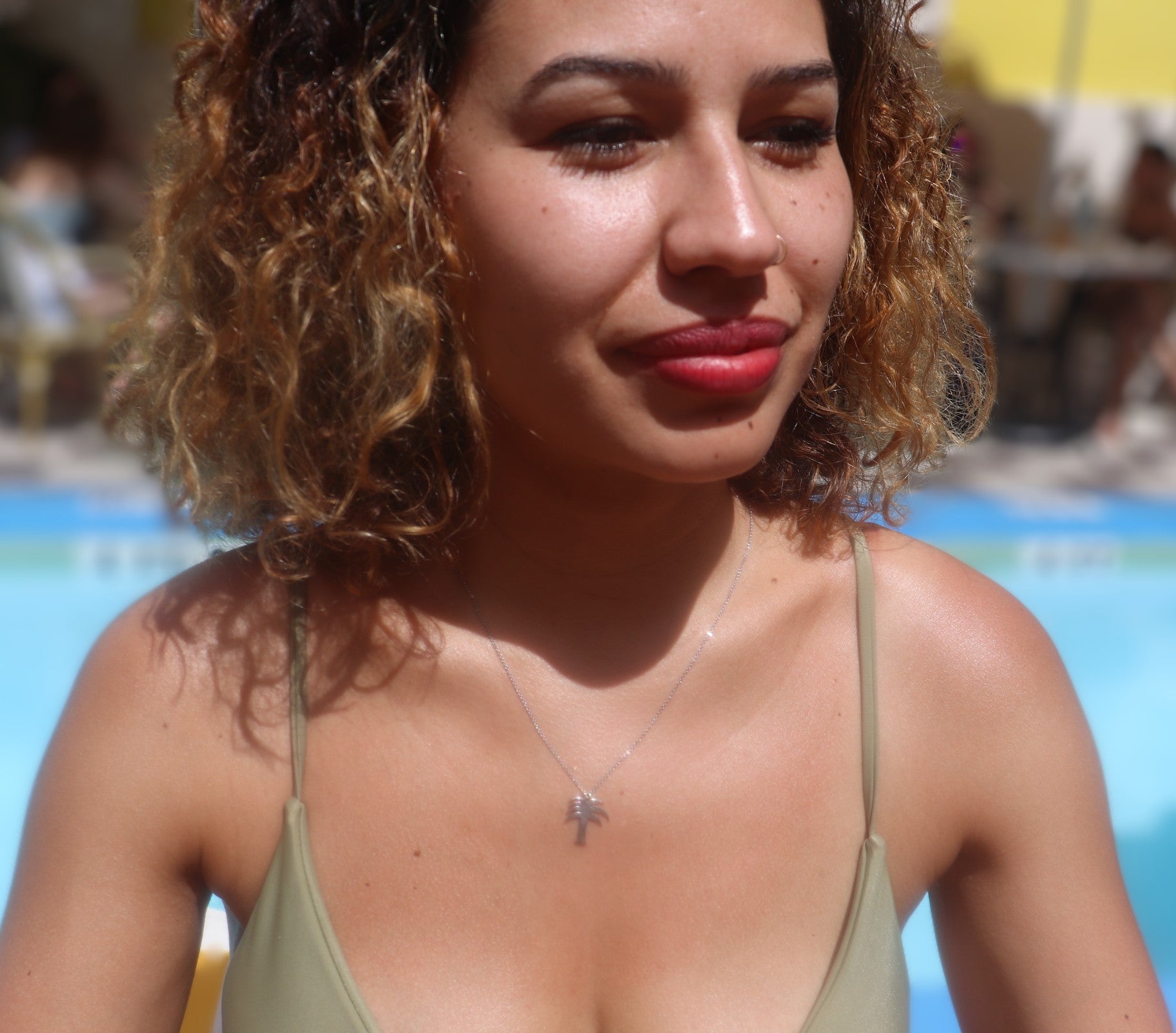 woman at pool with shoulder length curly hair and wearing a green bikini and a mini palm tree necklace from the wandering jewel