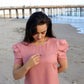 woman on beach in pink dress wearing a flower shaped necklace