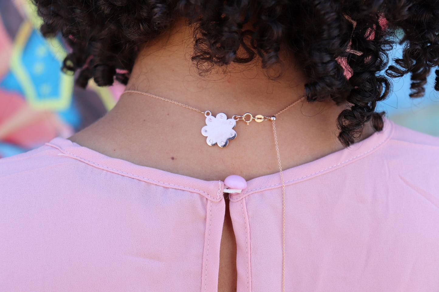 Back of neck view of woman in pink dress wearing Seven diamond logo plate on rose gold cloud with seven diamonds set evenly around the cloud from the wandering jewel