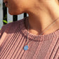 woman in pink shirt standing against a white picket fence  wearing a Jehovah coin necklace from the wandering jewel