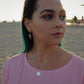woman on beach in pink shirt at golden hour wearing Jehovah coin necklace from the wandering jewel