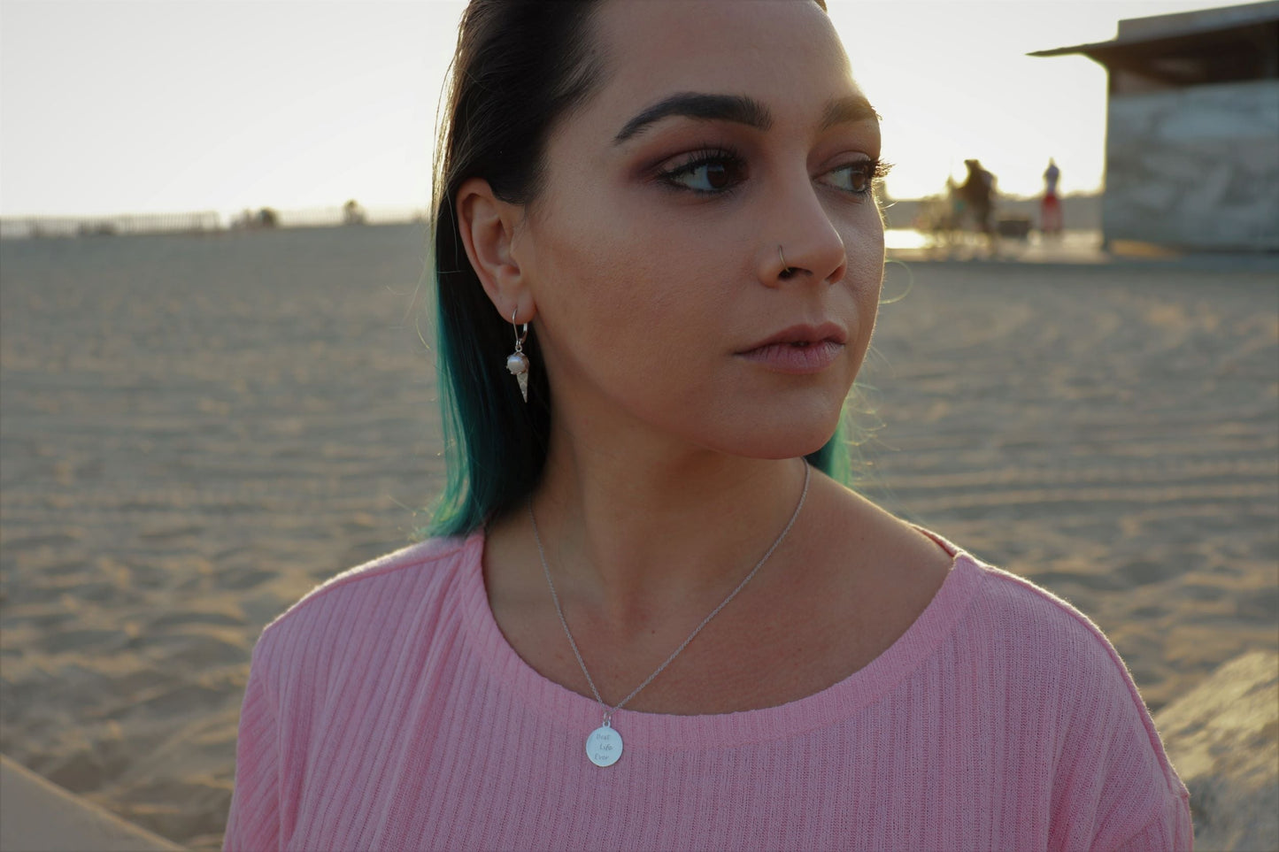 woman on beach in pink shirt at golden hour wearing Jehovah coin necklace