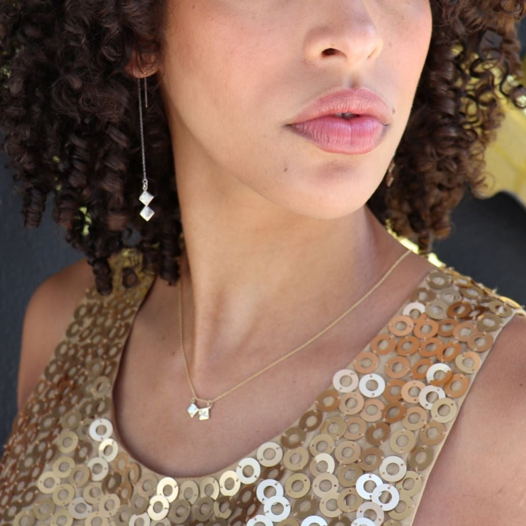 black woman with curly hair in gold sequin dress wearing gold dice earrings and matching necklace