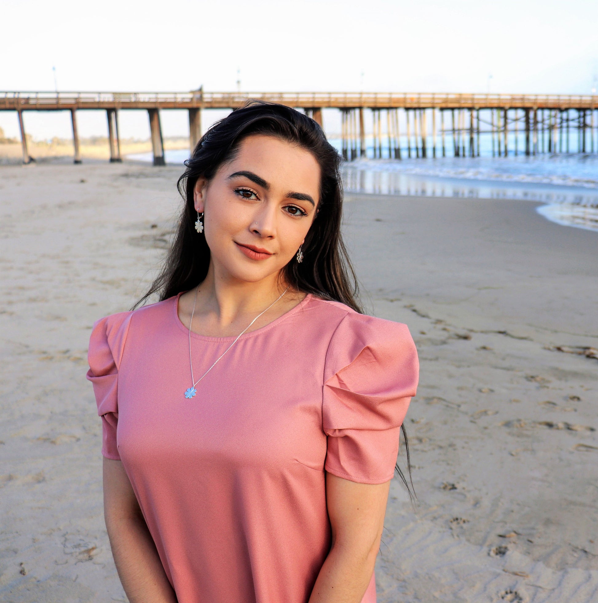 woman in a pink dress on beach wearing flower earrings and a matching necklace