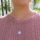 woman in pink shirt standing in front of a white picket fence wearing flower pendant necklace