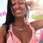 black woman on beach in pink bikini in front of a lifeguard stand wearing goaldigger necklace
