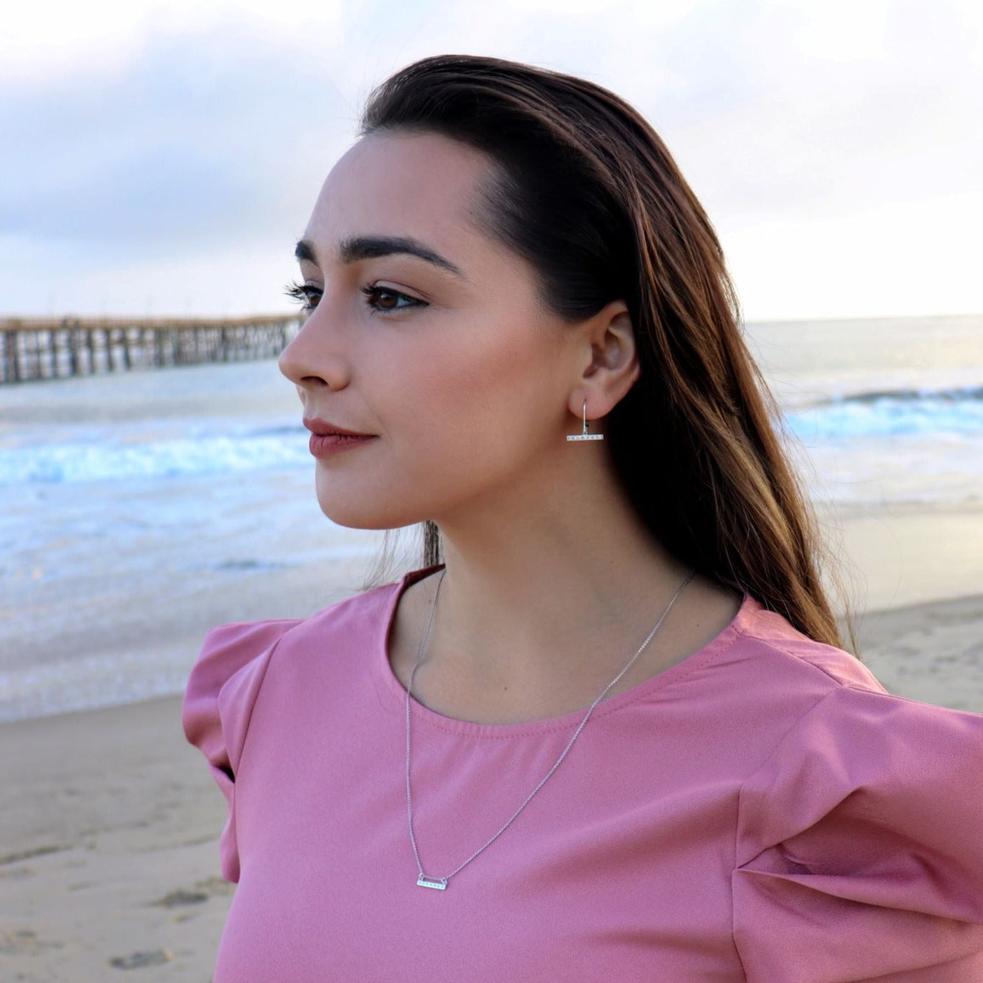 woman in pink dress on the beach wearing diamond bar earrings
