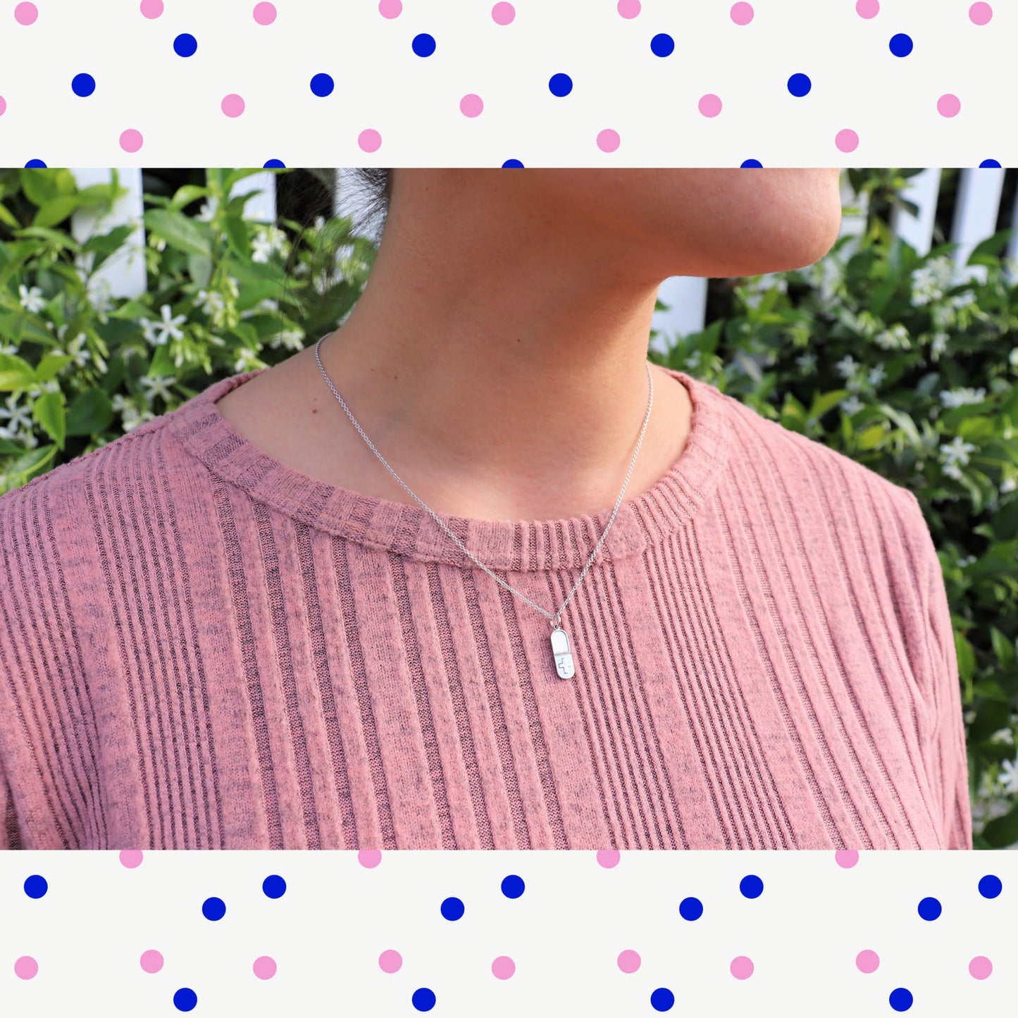 woman in pink shirt in front of white picket fence in garden wearing a tiny pill  shaped pendant necklace from the wandering jewel