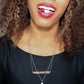 black woman with curly hair in a black dress with pill in her mouth wearing a necklace that says medicated