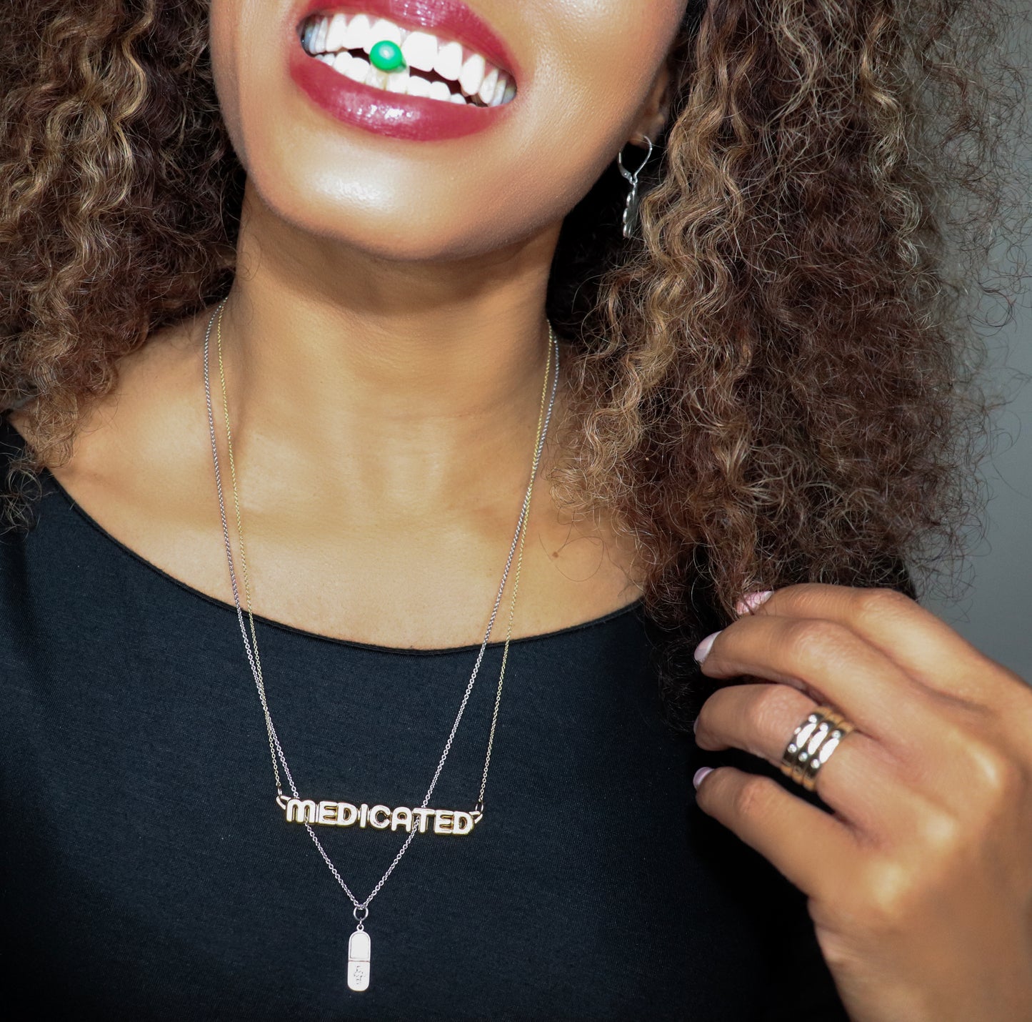 black woman in a black dress with green  pill in her mouth wearing a gold necklace that says medicated