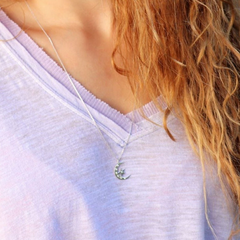 blonde Woman wearing a purple shirt and a diamond  moon and star pendant