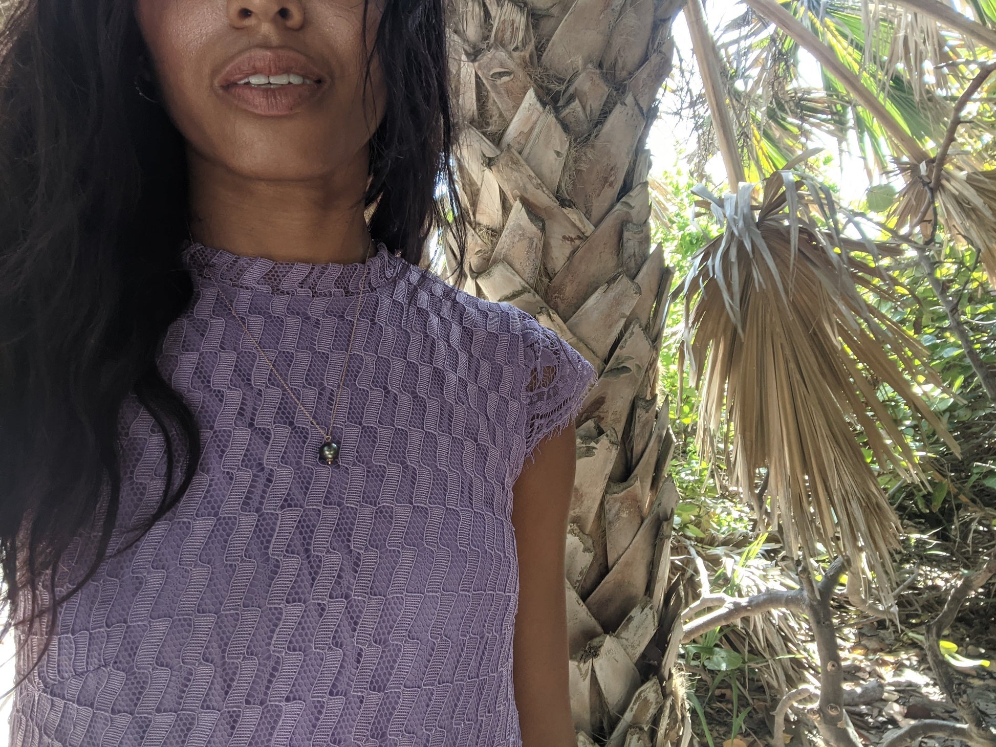 black woman with curly hair in purple dress wearing black pearl pendant on rosegold chain from the wandering jewel