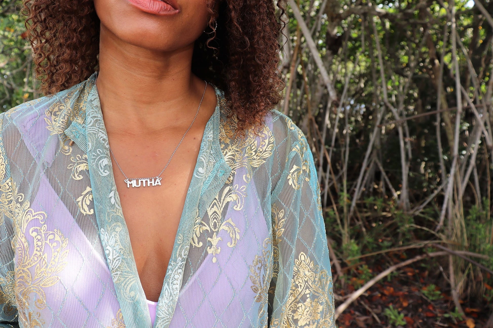 black woman in forest wearing a green and purple blouse over a lavender tank wearing mutha mother necklace from the wandering jewel