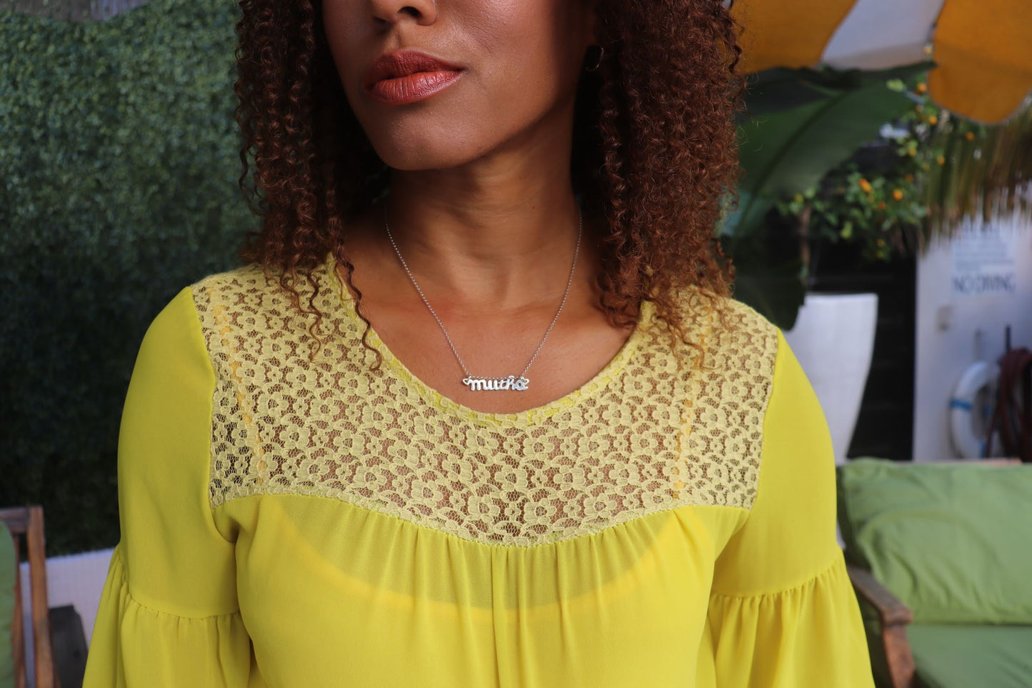 black woman with curly hair in a yellow dress at pool wearing silver mutha mother necklace