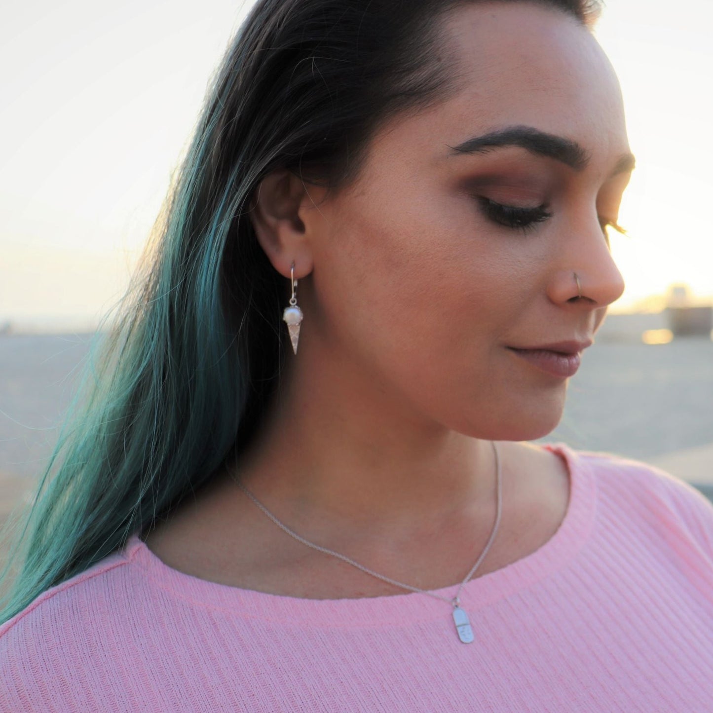 woman in pink shirt with blue hair at beach wearing a pill shaped pendant necklace