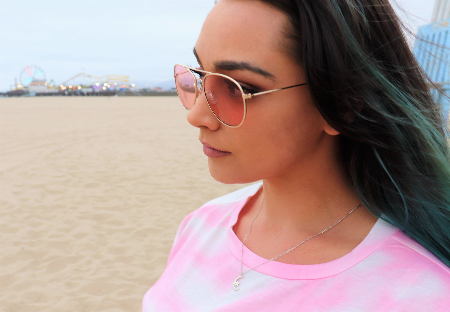  woman at beach with sunglasses and pink tie-dye shirt wearing sun and moon diamond pendant from the wandering jewel