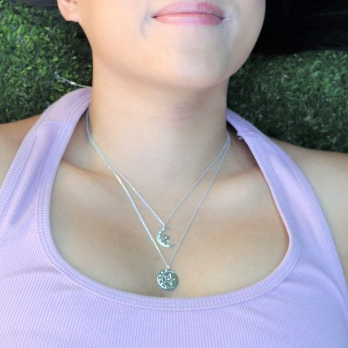 woman lying down in the grass and wearing a white tank top and diamond moon and star pendant necklace from the wandering jewel