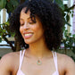 black woman with curly hair smiling and looking to her right in white sports bra wearing jade ring necklace 