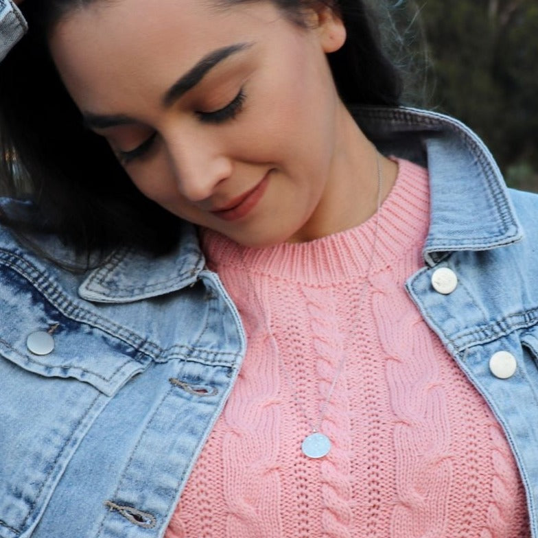  woman in pink sweater and light blue denim jacket wearing a diamond coin necklace from the wandering jewel