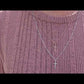 video of woman in pink sweater standing in front of a white picket fence and white roses wearing two 7 diamond cross necklaces from the wandering jewel