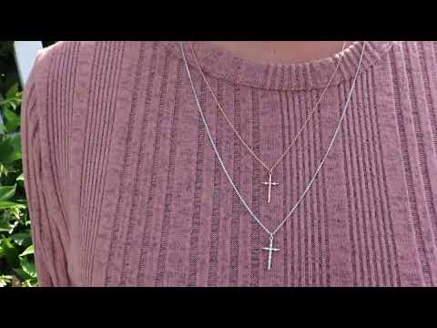 woman in pink sweater wearing two tiny crosses, one is in rose gold and the other is in silver both are from the wandering jewel