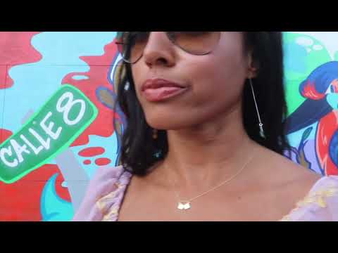 woman in pink blouse and sunglasses standing in front of a graffiti wall wearing a dice necklace and matching earrings from the wandering jewel