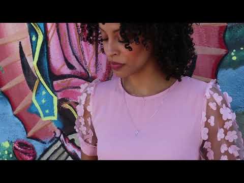 video of black woman with curly hair and a pink dress wearing two 7 diamond cross necklaces from the wandering jewel