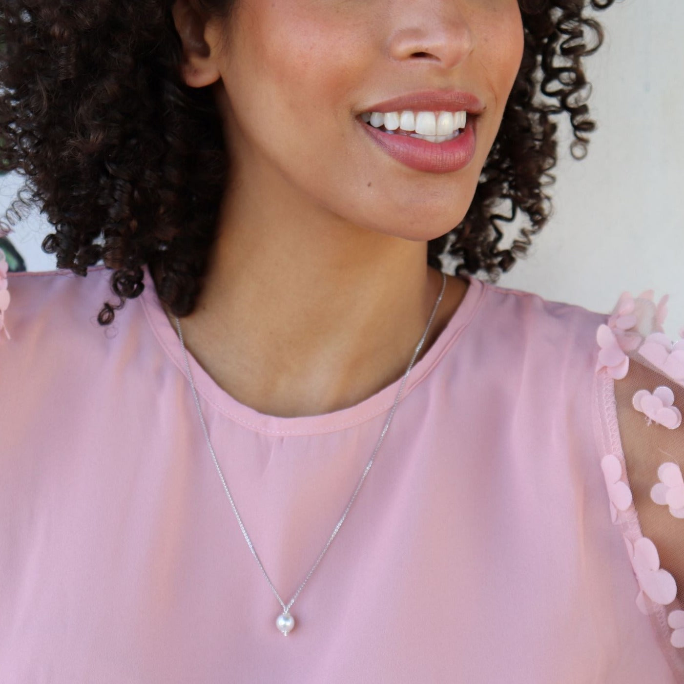 black woman with curly hair in pink dress wearing a white pearl pendant necklace
