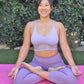 woman in purple sports bra and leggings, sitting in yoga lotus pose wearing diamond lotus neckalce