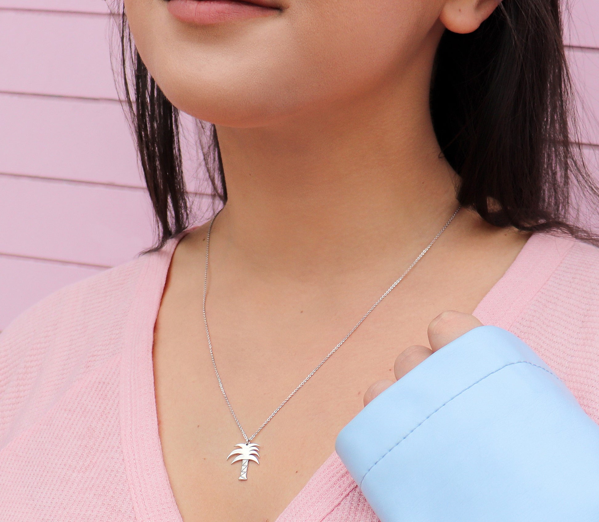 brunette woman wearing a pink t shirt and blue jean jacket  and a mini palm tree necklace from the wandering jewel