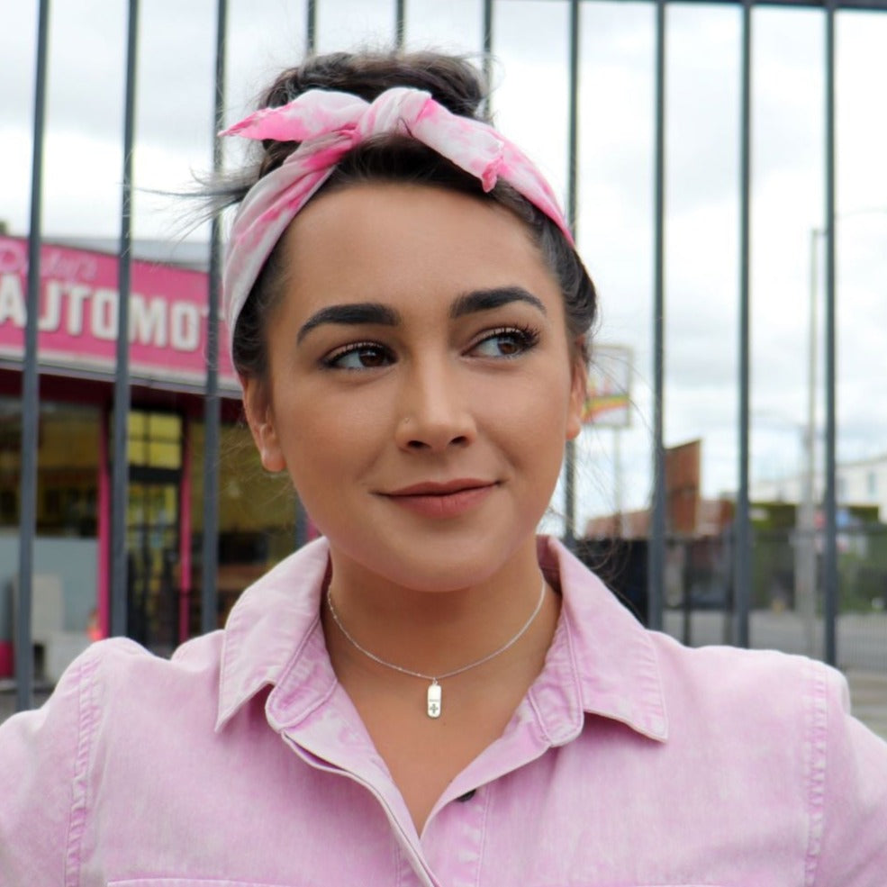 woman in pink jumpsuit with a pink headband in front of automotive store wearing a diamond pill necklace