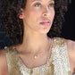 black woman with curly hair in gold sequin dress wearing gold pearl pendant