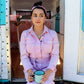 woman drinking tea in pink jumpsuit in the back of a blue and pink mini trailer and wearing a silver teacup pendant necklace