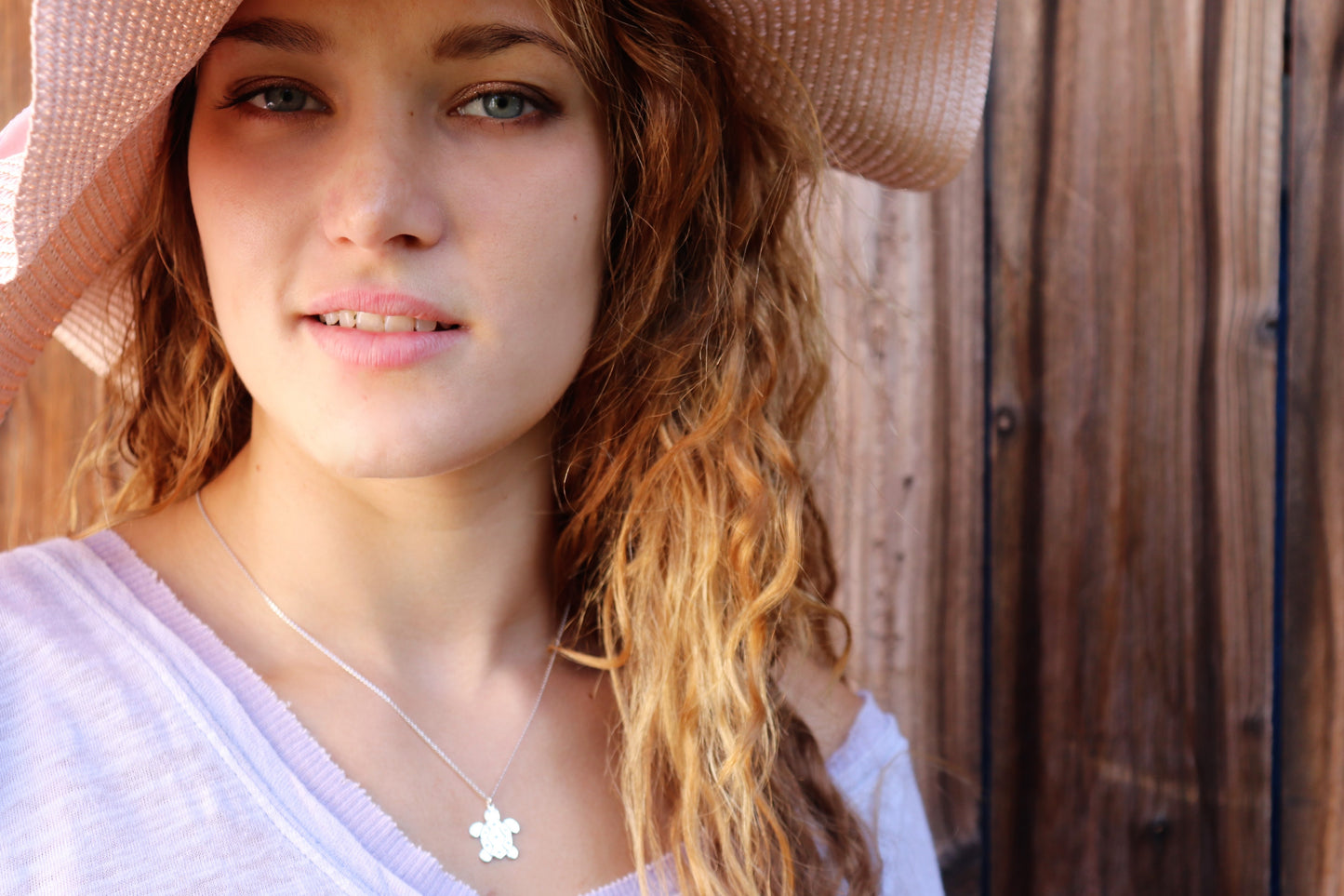 Diamond turtle necklace on woman wearing a straw hat and t-shirt
