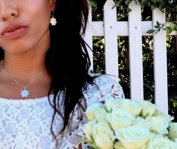 woman in bridal dress standing in front of white picket fence wearing flower pendant and matching earrings from the wandering jewel