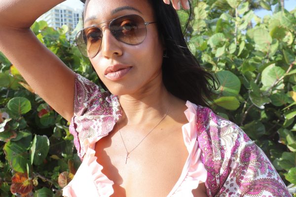 woman on beach in sunglasses, pink top and pink paisley shirt wearing a 7 diamond cross from the wandering jewel