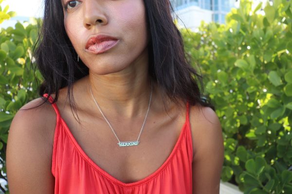 woman in orange top sitting in a garden and wearing a the herkind nameplate necklace from the wandering jewel