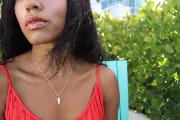 woman sitting on rooftop in orange tank top wearing a silver pill pendant from the wandering jewel