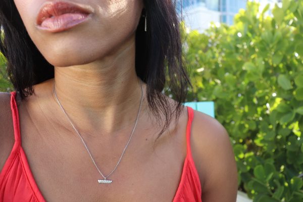 black woman in orange top in garden wearing the 7 diamond heart pendant from the wandering jewel