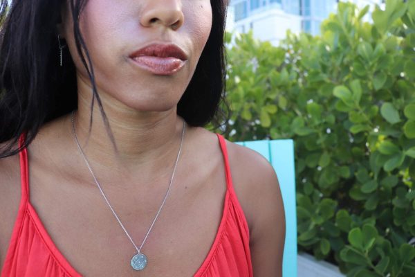 black woman in orange dress in garden wearing  the 7 diamond coin necklace from the wandering jewel