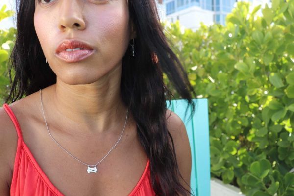 woman in orange top sitting in garden and wearing the double 7 necklace from the wandering jewel