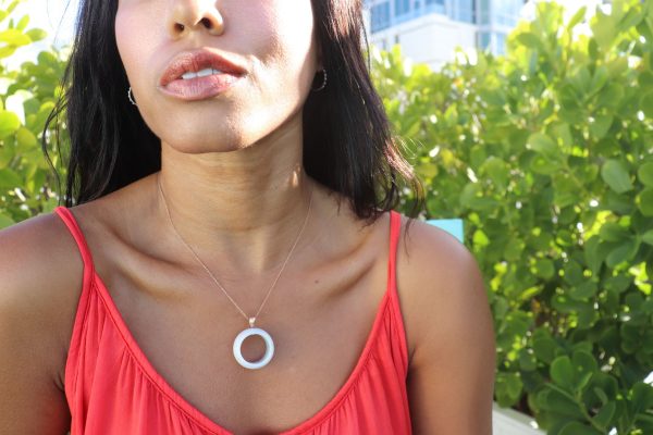 woman sitting in a rooftop garden in a bright orange dress wearing white jade ring necklace from the wandering jewel